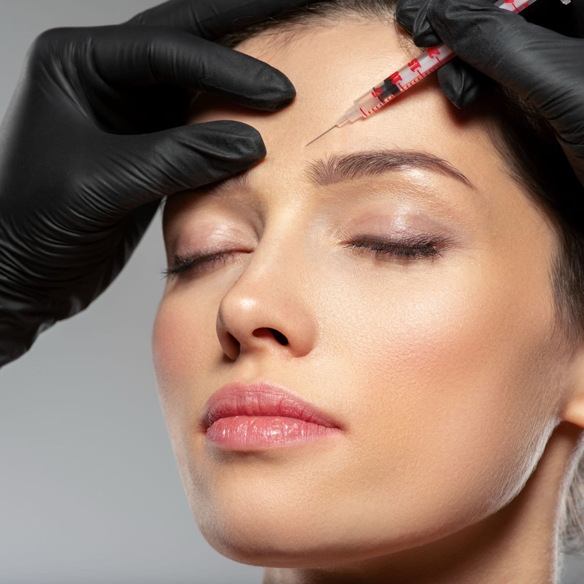 Gloved hands give a small injection in a woman’s forehead