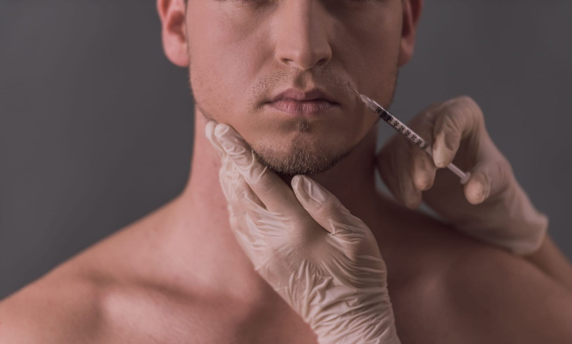Gloved hands give an injection near a man’s jaw