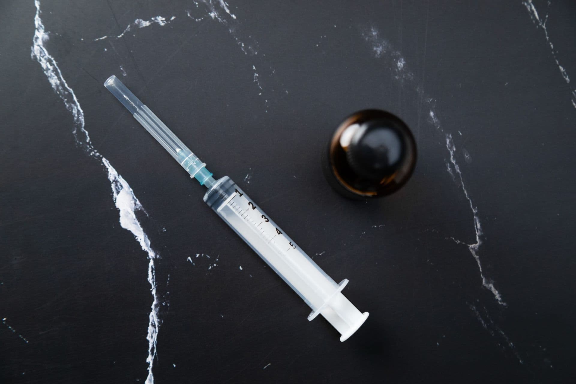 A syringe and a small amber bottle on dark marble